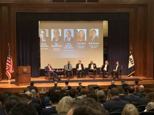 Secretary Ross seated on stage with five panelists in front of large audience