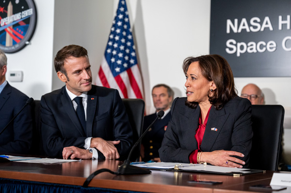 French President Emmanuel Macron (seated, left) listens to Vice President Kamala Harris (seated, right) speaking with American flag and NASA Headquarters sign behind them
