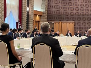 Attendees sitting around a round table listen to a presented speaking into a hand mic