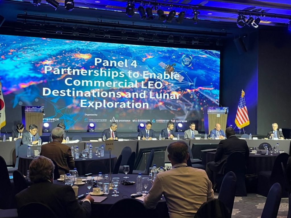 Richard DalBello (far right) moderates a panel of seated speakers with a colorful graphic backdrop reading “Panel 4 | Partnerships to Enable Commercial LEO Destinations and Lunar Exploration”