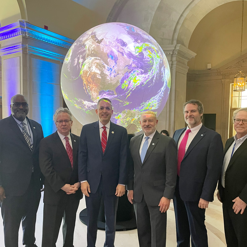 Group of men standing in front of enormous Earth globe 