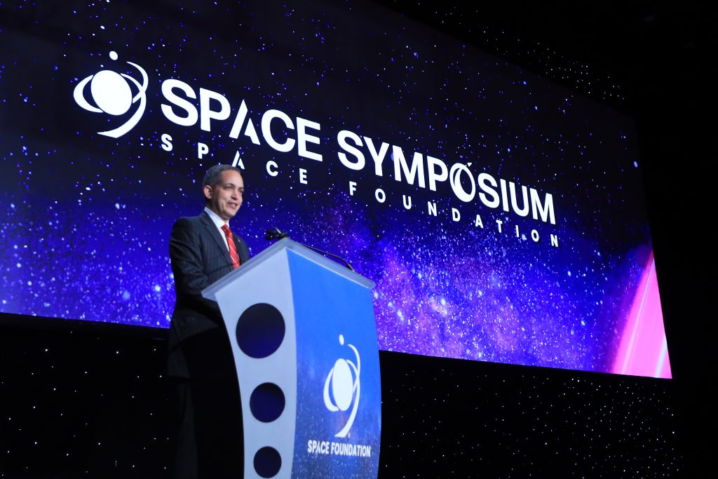 Deputy Secretary Don Graves smiling at podium with starry background reading "Space Symposium | Space Foundation"