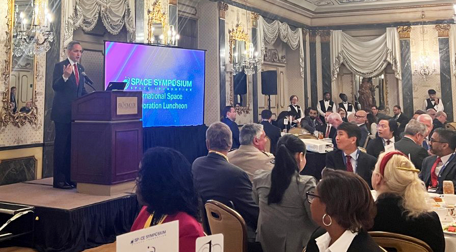 Deputy Secretary Graves gesturing at podium on stage in front of seated audience in fancy dining room