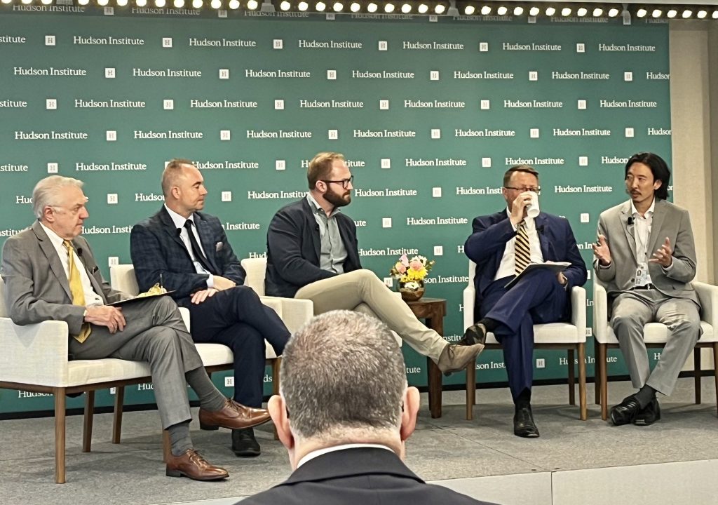 Jason Kim (far right) gestures while speaking with four men seated before a green backdrop